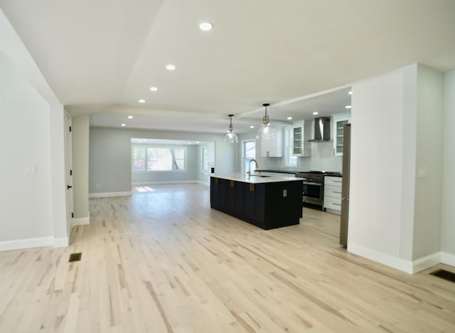 kitchen featuring wall chimney range hood, a sink, high end range, open floor plan, and a center island with sink