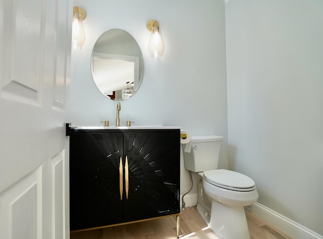 half bath with vanity, baseboards, wood finished floors, and toilet