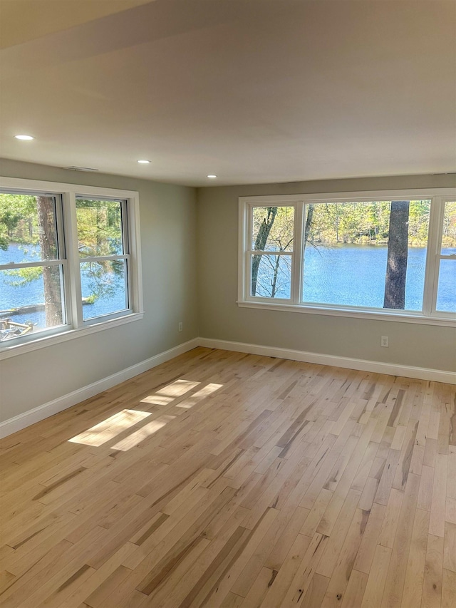spare room with recessed lighting, baseboards, a water view, and light wood-style floors