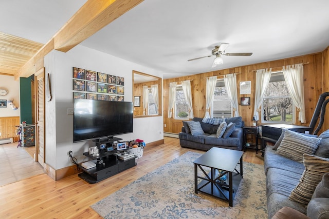 living area with baseboards, wood walls, ceiling fan, and a baseboard heating unit