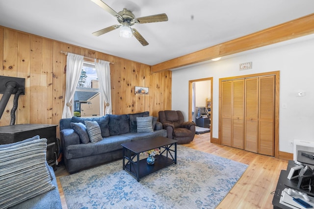 living room featuring wooden walls, a ceiling fan, wood finished floors, and a wood stove