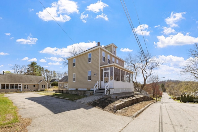 view of property exterior featuring a chimney, a sunroom, and aphalt driveway