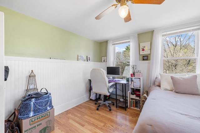 bedroom with a baseboard radiator, a ceiling fan, wainscoting, and wood finished floors