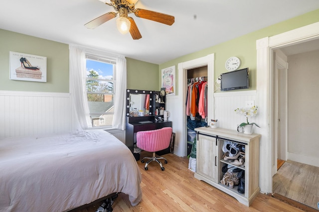 bedroom with light wood finished floors, ceiling fan, a wainscoted wall, and a spacious closet