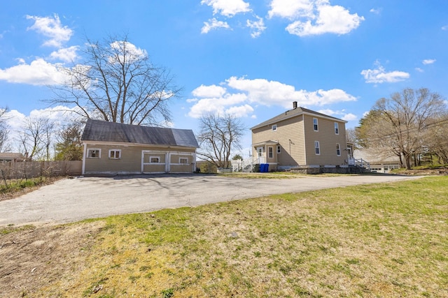 rear view of property featuring fence, an outdoor structure, a yard, and aphalt driveway