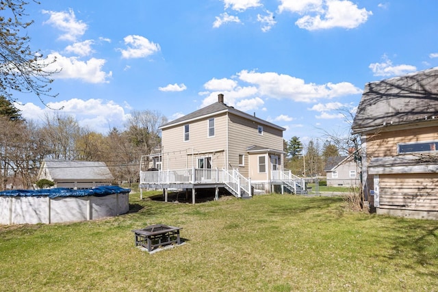 rear view of house featuring a covered pool, a deck, a yard, a fire pit, and stairs
