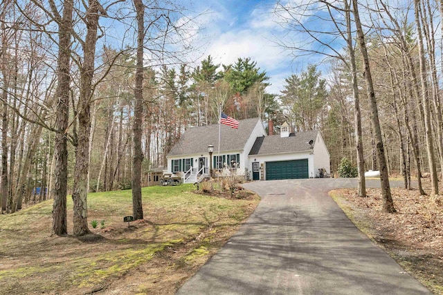 cape cod home with a shingled roof, an attached garage, driveway, and a front yard