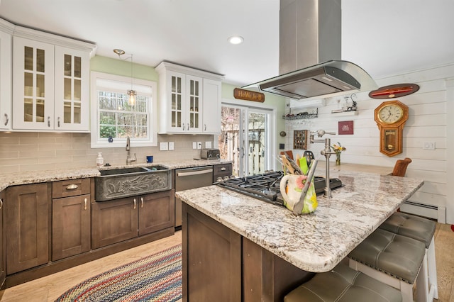 kitchen featuring a sink, a breakfast bar, island range hood, and light stone counters