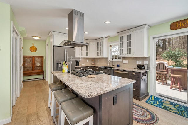 kitchen with appliances with stainless steel finishes, white cabinets, light stone countertops, and island range hood