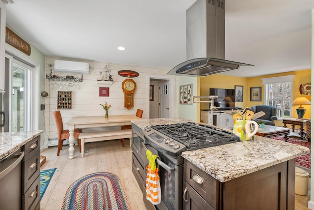 kitchen with dark brown cabinetry, island exhaust hood, stainless steel range with gas stovetop, light stone counters, and light wood finished floors