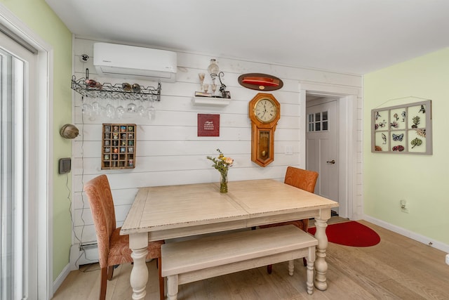 dining room featuring baseboards, a wall unit AC, and light wood-style flooring