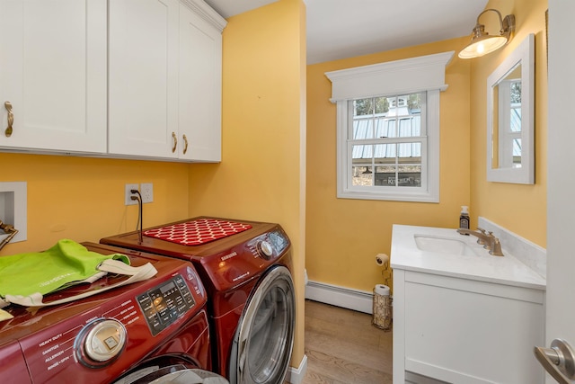 laundry area featuring wood finished floors, a baseboard radiator, washing machine and clothes dryer, a sink, and cabinet space
