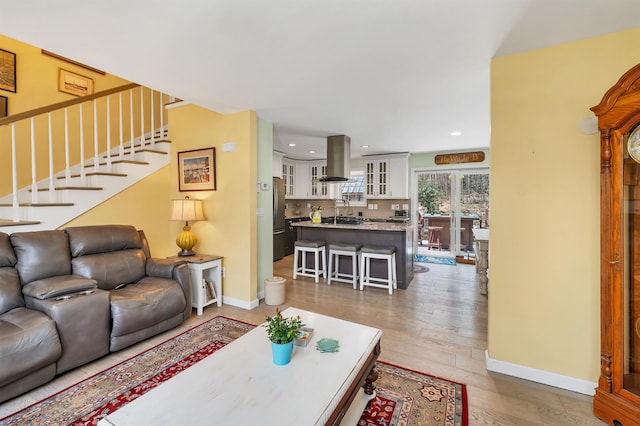 living room featuring stairs, recessed lighting, baseboards, and light wood-style floors