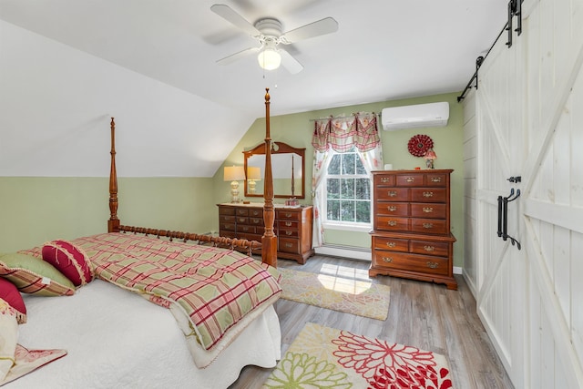 bedroom featuring wood finished floors, a barn door, a baseboard heating unit, a wall unit AC, and vaulted ceiling
