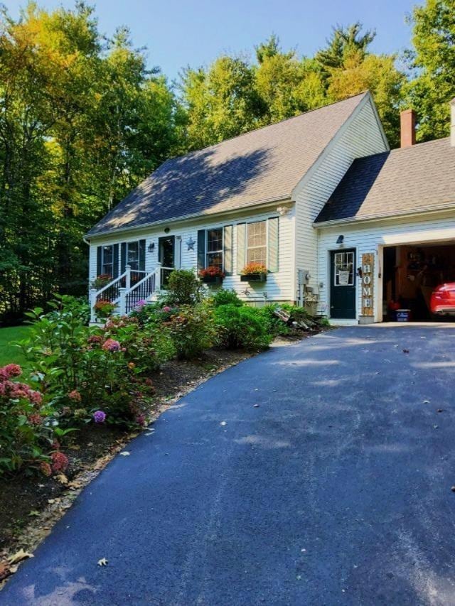 single story home featuring a garage, driveway, a chimney, and a shingled roof