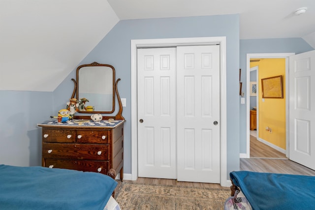 bedroom with baseboards, vaulted ceiling, wood finished floors, and a closet