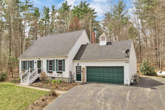 cape cod-style house featuring roof with shingles, an attached garage, a chimney, and driveway