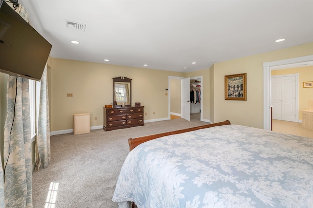 bedroom with a walk in closet, light colored carpet, recessed lighting, and visible vents