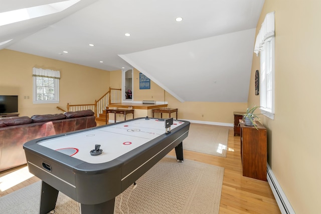 playroom with vaulted ceiling with skylight, baseboard heating, baseboards, light wood-style floors, and recessed lighting