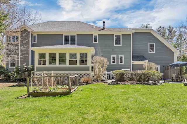 back of house with a shingled roof, a yard, and a garden