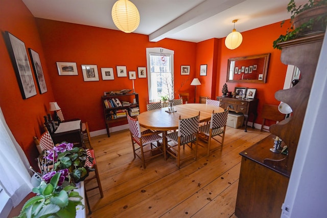 dining room with baseboards, light wood-style flooring, and beamed ceiling