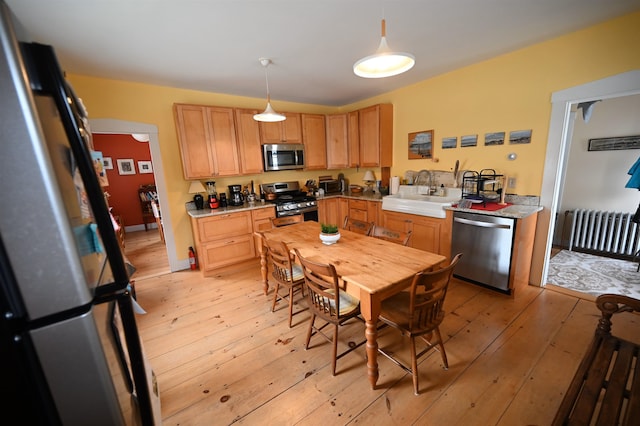 kitchen featuring appliances with stainless steel finishes, hanging light fixtures, a sink, light wood finished floors, and radiator