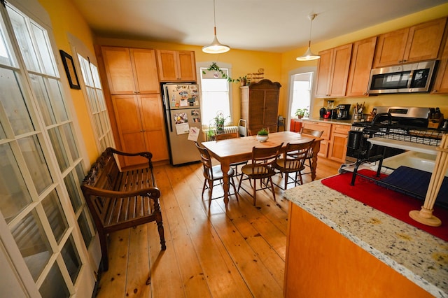 kitchen featuring brown cabinets, appliances with stainless steel finishes, hanging light fixtures, and light wood finished floors