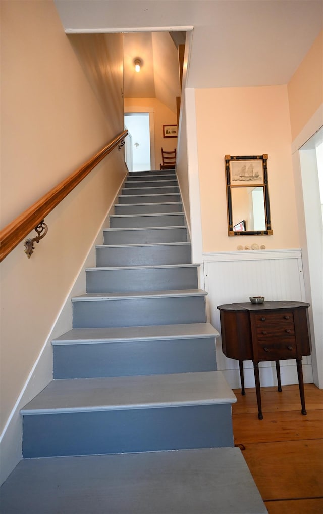staircase with wood finished floors and a wainscoted wall