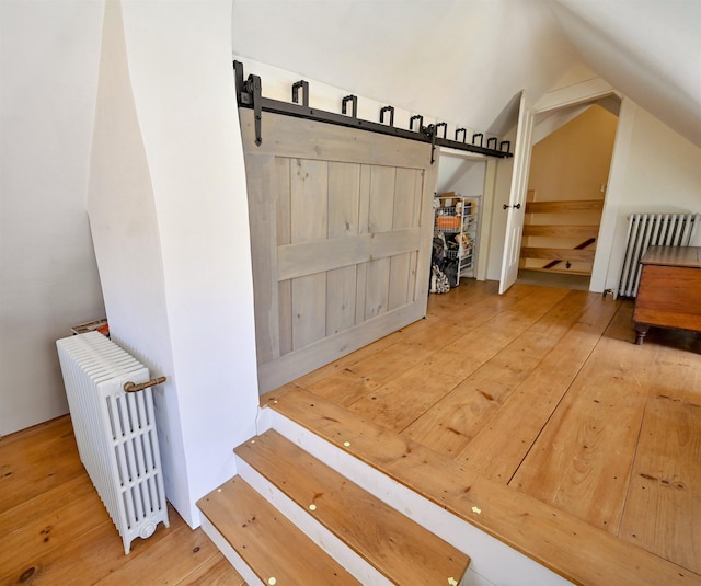 additional living space featuring vaulted ceiling, a barn door, stairway, wood-type flooring, and radiator heating unit