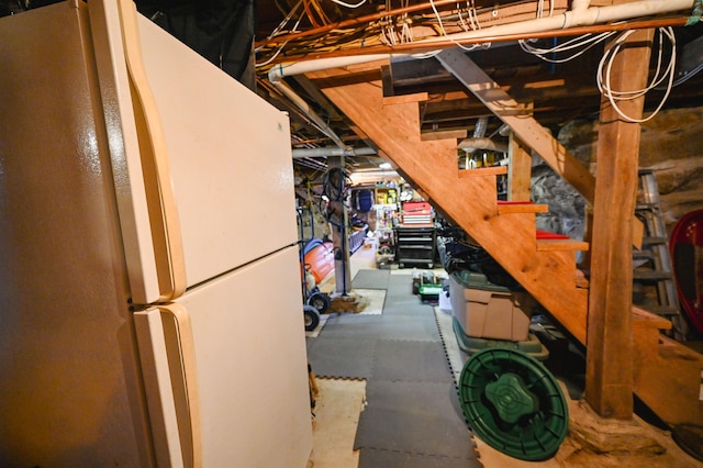 unfinished below grade area featuring freestanding refrigerator and stairs
