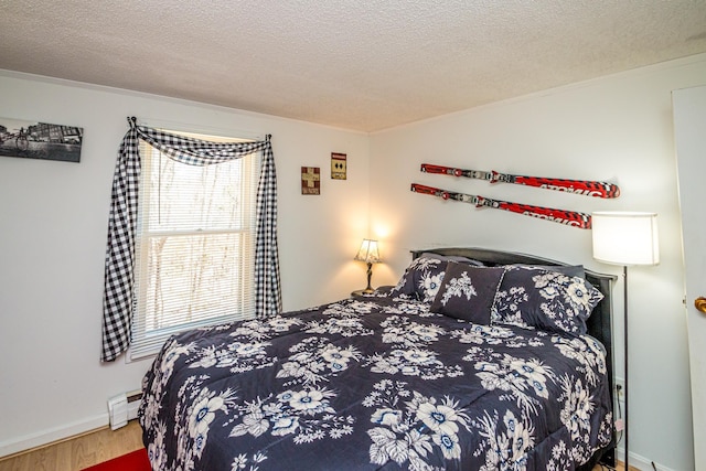 bedroom featuring crown molding, baseboard heating, a textured ceiling, and wood finished floors