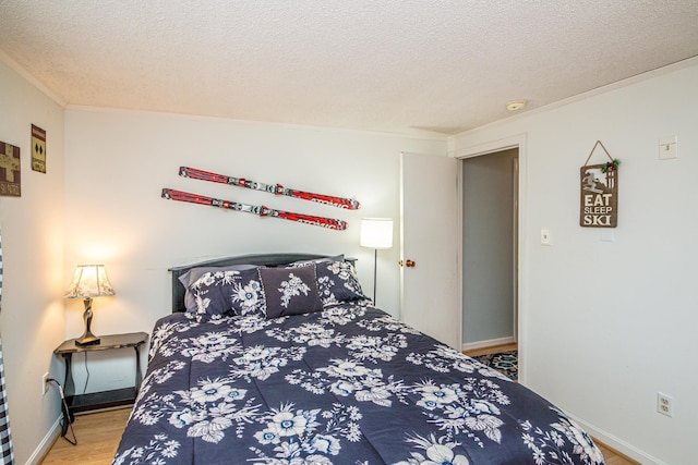 bedroom with crown molding, baseboards, a textured ceiling, and wood finished floors