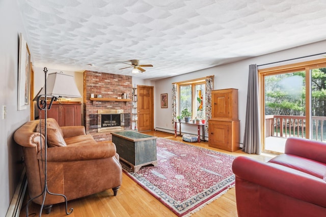living area with baseboard heating, ceiling fan, wood finished floors, and a fireplace