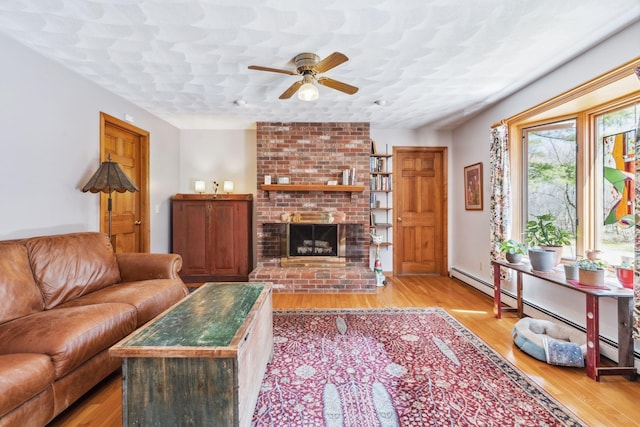 living area featuring light wood-style floors, a ceiling fan, baseboard heating, and a fireplace