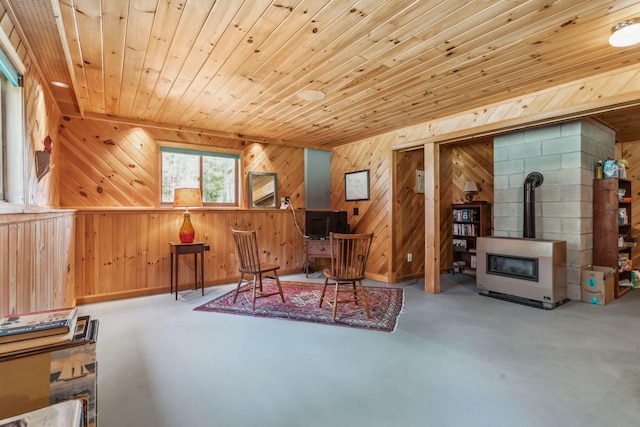 living area with wood walls, concrete floors, wood ceiling, and a wood stove