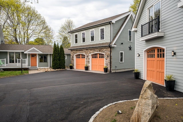 view of front of home with a garage, stone siding, a balcony, and driveway