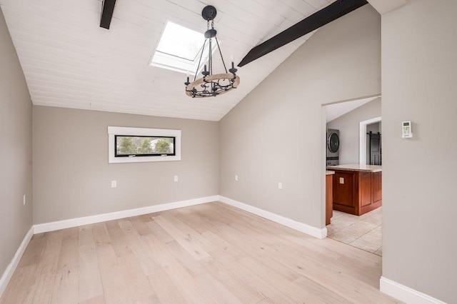 spare room with baseboards, stacked washer / dryer, vaulted ceiling with skylight, and light wood-style floors