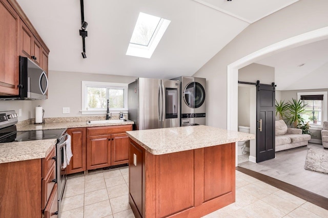 kitchen featuring appliances with stainless steel finishes, stacked washer / drying machine, a sink, light countertops, and lofted ceiling with skylight