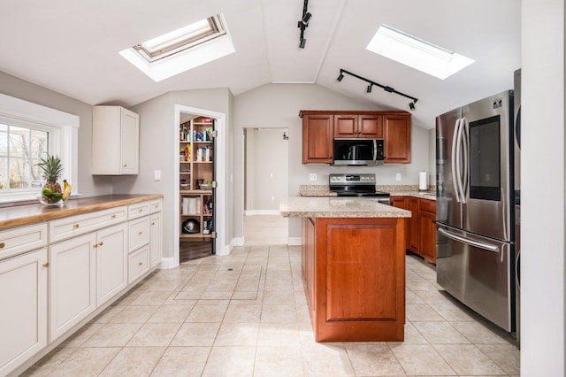 kitchen with light tile patterned flooring, track lighting, vaulted ceiling with skylight, stainless steel appliances, and a kitchen island