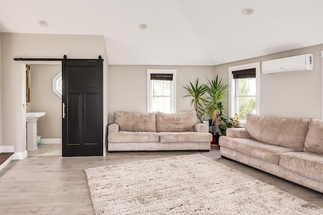 living room featuring a barn door, baseboards, a wall unit AC, lofted ceiling, and light wood-type flooring