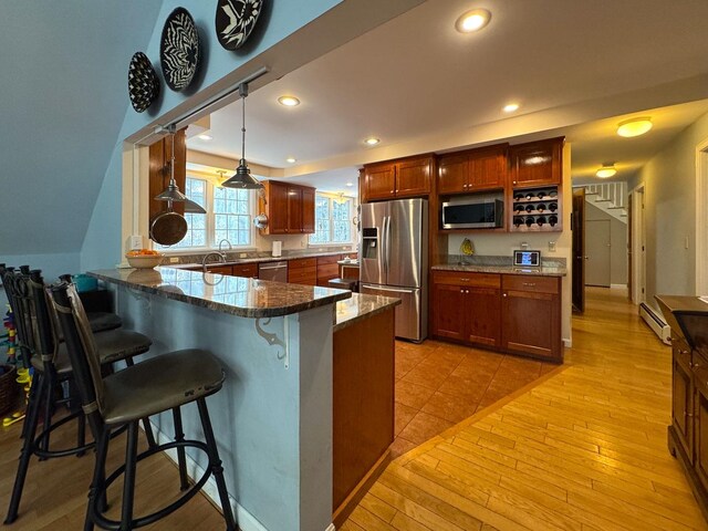 kitchen with appliances with stainless steel finishes, dark stone countertops, a peninsula, a breakfast bar, and light wood-style flooring