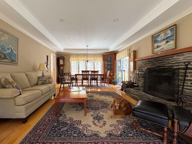 living room featuring crown molding, an inviting chandelier, a stone fireplace, and wood finished floors