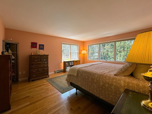bedroom with light wood-style floors, baseboards, and a baseboard heating unit