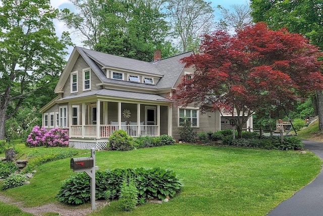 view of front of property featuring a shingled roof, a chimney, a porch, and a front lawn