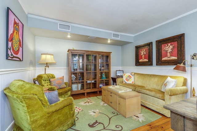 living room featuring a wainscoted wall, ornamental molding, hardwood / wood-style flooring, and visible vents