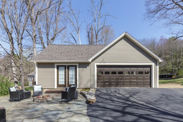 exterior space with an attached garage, a shingled roof, an outdoor living space with a fire pit, and driveway