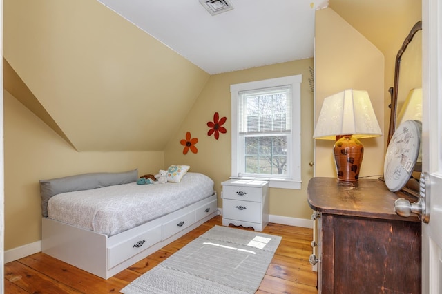bedroom with baseboards, vaulted ceiling, light wood finished floors, and visible vents