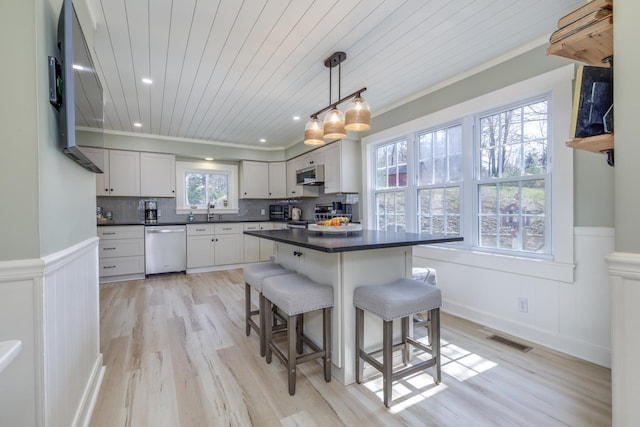 kitchen featuring a kitchen breakfast bar, visible vents, dark countertops, a wainscoted wall, and stainless steel appliances