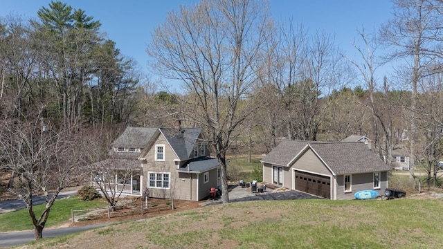 exterior space with a detached garage, a lawn, an outbuilding, and a shingled roof