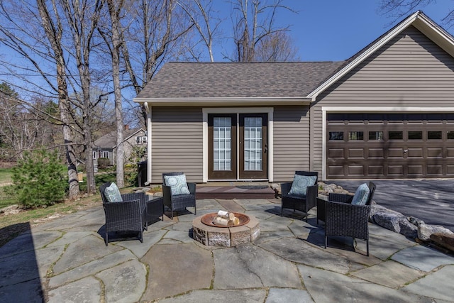 view of patio with an attached garage, driveway, and an outdoor living space with a fire pit